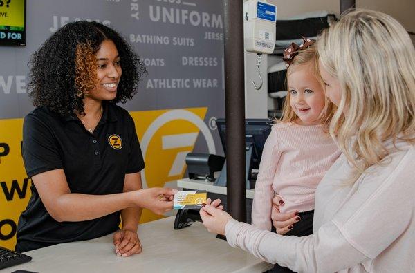 A happy mom holding a child hands a friendly ZIPS Team Member a ZIPS Gift Card. ZIPS Cleaners is a mom's best friend, and so ...