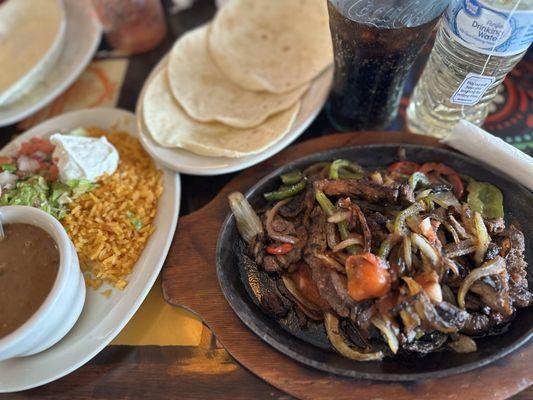 Steak fajitas with red & green bell peppers, onions, tortillas, beans, rice, guacamole, pico de gallo, sour cream, and queso, chips, & Coke.