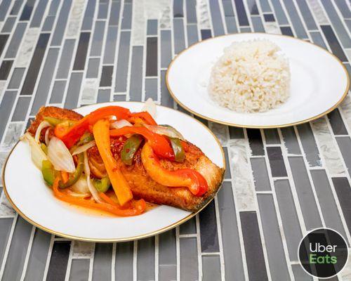 Salmon in a sweet chili sauce garnished with onions peppers and carrots served with white rice