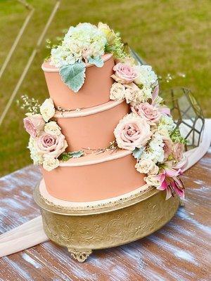 3 tiered wedding cake adorned with a variety of fresh flowers and greenery