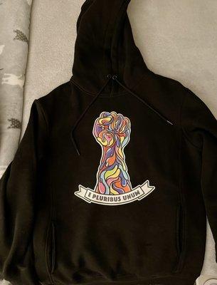 Black pullover hoodie with raised fist in a multitude of colors and the phrase "E Pluribus Unum."