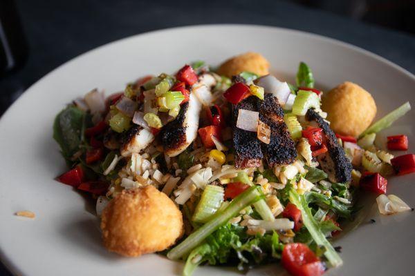 BLACKENED CHICKEN SALAD: Spring mix greens, blackened chicken breast, white cheddar, dirty rice, sautéed trinity vegetables, grape tomatoes.