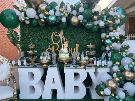 Grass wall, oh baby sign, cake stands, baby table, leaves and ballon garland, white and gold love seat all supplied by Majestic.