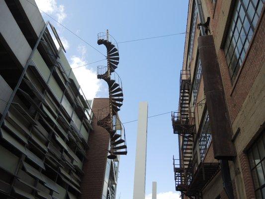 Spiral fire escape sculpture titled Architectural DNA between buildings