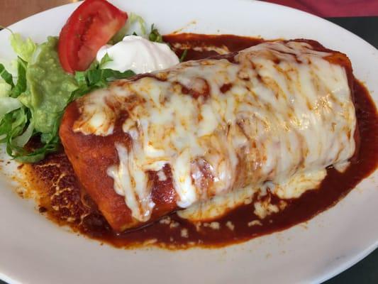 Carne asada burrito topped with red sauce and bubbly melted cheese.