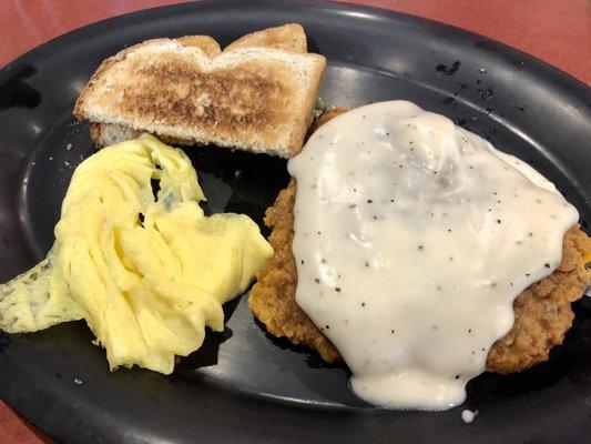 Chicken Fried Steak Breakfast with a hand breaded small chicken fried steak, smothered in gravy, two eggs (scrambled), and wheat toast.