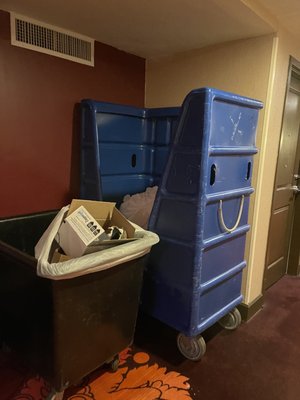 Trash  and linen bins in the hall. Late at night.