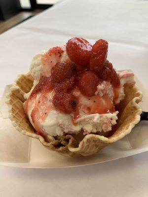 Strawberry cheesecake ice cream with strawberry topping in a waffle bowl.