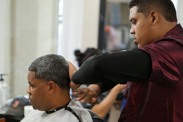 Owner michaelangelo preforming men's haircut on a patron.