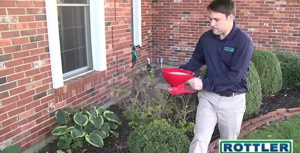 Rottler technician spreading a granular pest treatment about the perimeter of a home.