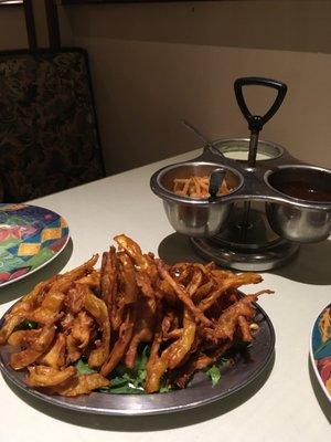 Vegetarian mixed platter.  One samosa, one chunk of paneer cheese, and multiple fried pieces with dipping sauces and onions