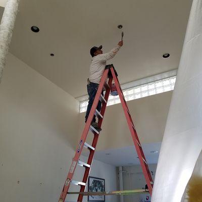 Cartelli Painting Co. cutting in around recessed lighting in ceiling.