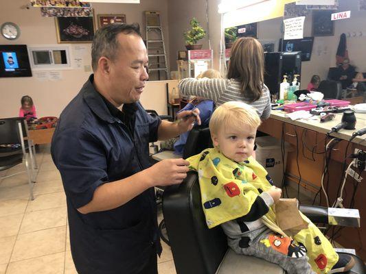 Kiddo with a bag of popcorn and Curious George getting a big boy hair cut with this kind man.