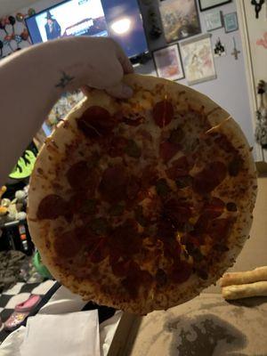 Three meat pizza being held up in the air with one hand.