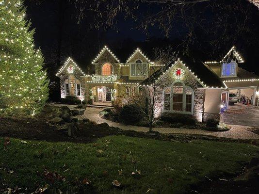 We outlined the rooflines, windows, and front evergreen in with warm white lights and added wreaths with big red bows.