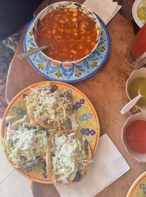 A bowl of Posole and 3 tostadas with beans, lettuce, cheese and crema.