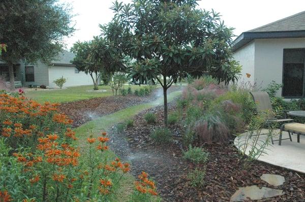 Sprinklers water a grass path that leads to a beautiful butterfly garden