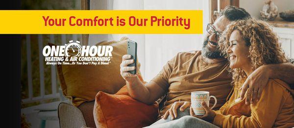 Couple sitting on a couch looking at a phone, drinking coffee, & smiling with the overlay text that says Your Comfort is Our ...