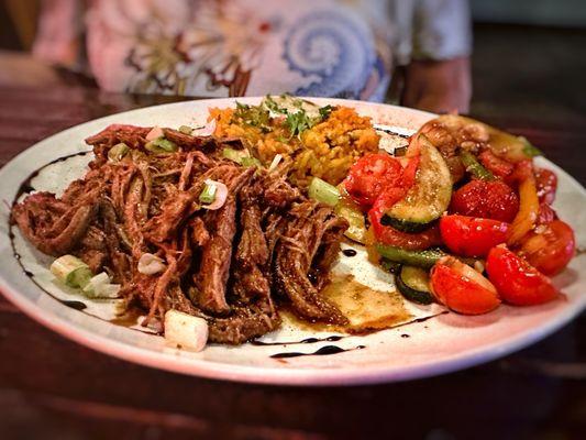 Ropa Vieja served with yellow rice and grilled vegetables.