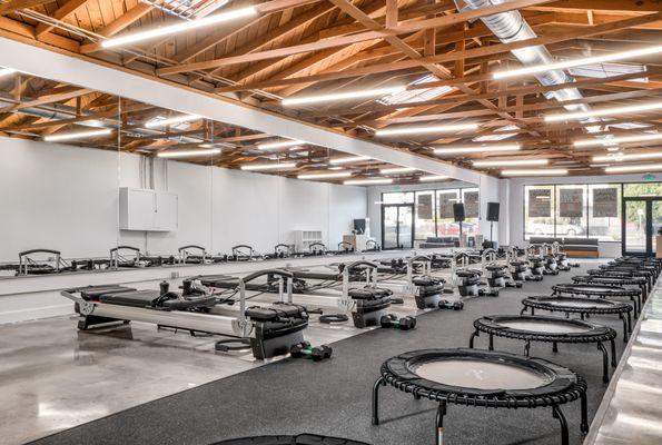 Sweat Pilates studio has reformer machines, trampolines, mirrored walls, and open wood-beamed ceilings in a sleek, modern space.