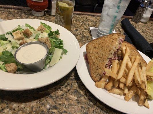 Caesar salad and Reuben sandwich with fries and a pickle.