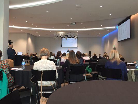 Odd "L" shaped conference room with video screens on 2 walls so that those sitting in the back recesses can see screens from everywhere.