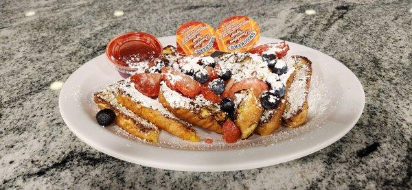 Three slices of french toast with strawberries, blueberries, powdered sugar, syrup, and strawberry compote.