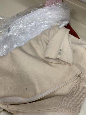 Beige sweater with black stains from dry cleaning