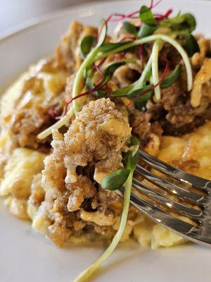 A piece of Fried Oyster with other fresh Oysters and Cheesy Polenta Grits in the background.