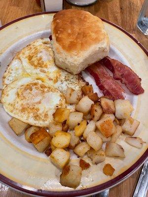 Breakfast plate with eggs cooked over medium, bacon and potatoes.