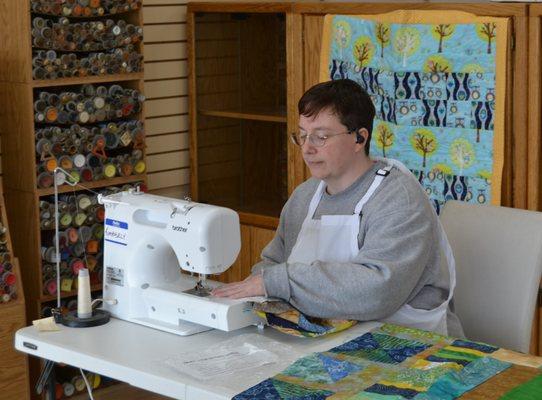 Kimberly sewing in front of a baby quilt and free-motion quilting example.