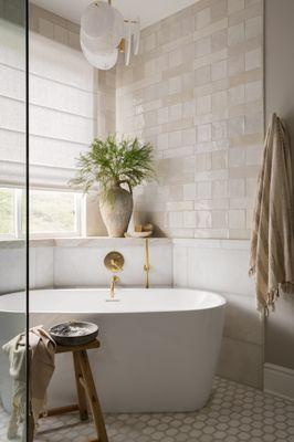 remodeled primary bath with freestanding bath tub, custom roman shade, brass plumbing fixtures, mosaic floor and chandelier