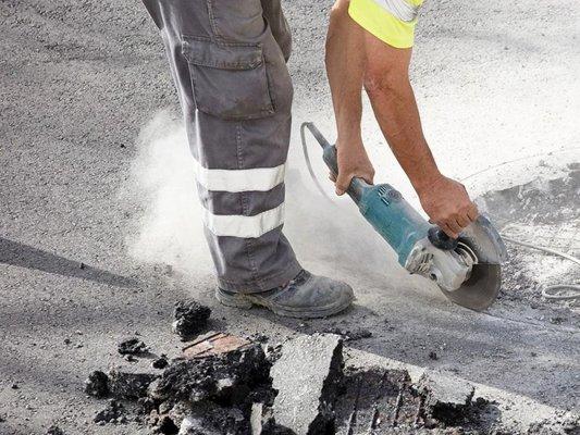 Worker using a power saw to cut through asphalt on a road