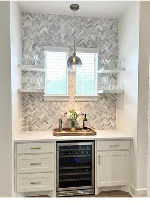 Wine bar with custom soft close cabinets with herringbone pattern backsplash, granite countertops and floating shelves.