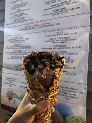 Blackberry ice cream topped with crushed Oreos in a waffle cone