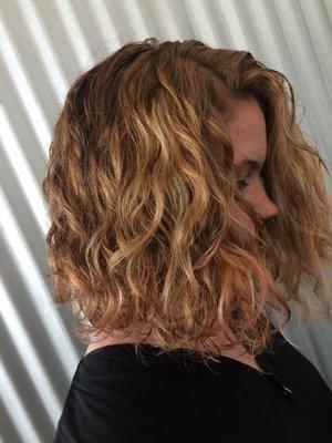 Shoulder-length loose layers and sunny-blonde hilites enhance her natural curls.