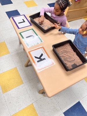 Children engaged using sensory bins for letter recognition.