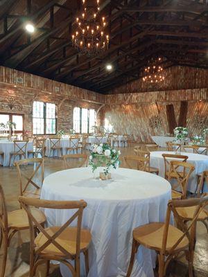 60" round tables, 120" round white poly tablecloth, acrylic crystal clear floral centerpieces, mercury votives, and wood cross-back chairs.