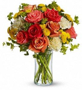 Dark orange, coral and orange roses, light yellow carnations, yellow button spray chrysanthemums and greens fill a slender gathering vase.