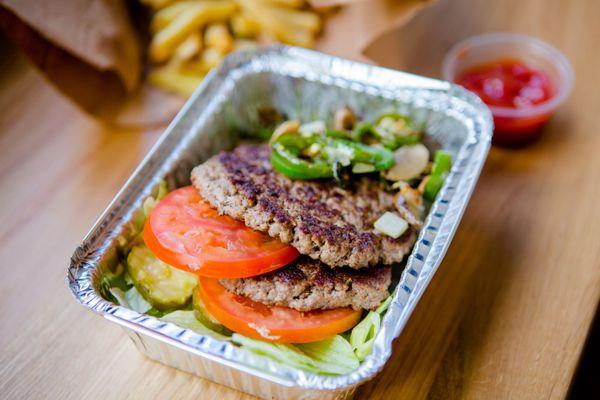 A photograph of the contents of a Five Guys burger bowl, which include two ground beef patties, tomatoes, jalapenos, lettuce ...