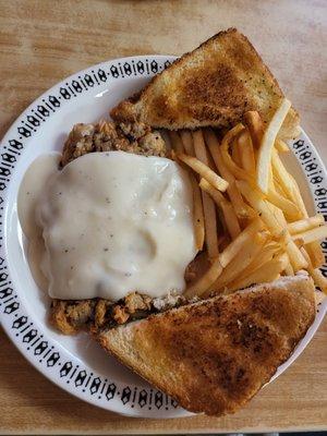 Chicken fried steak smothered in gravey with a pile of crispy French fries and two triangles of thick toast