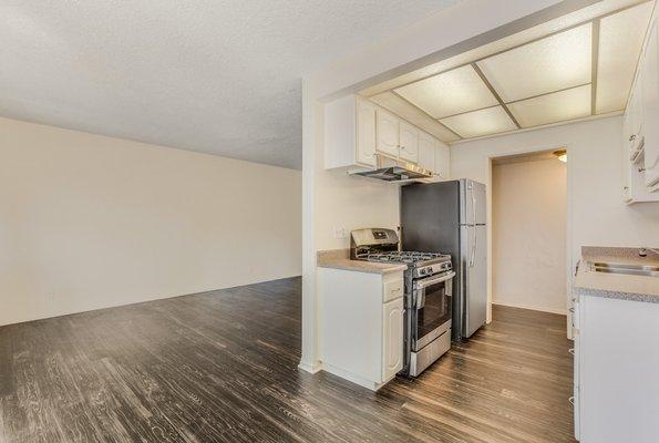 Living room and kitchen with hardwood style vinyl flooring and stainless steel appliances.