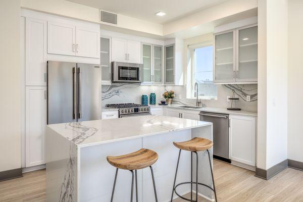 Modern kitchen with waterfall island, bar seating and marble style countertops and backdrops.