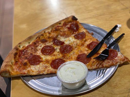 Single sliced pizza with a side of ranch. Hanging off the plate!