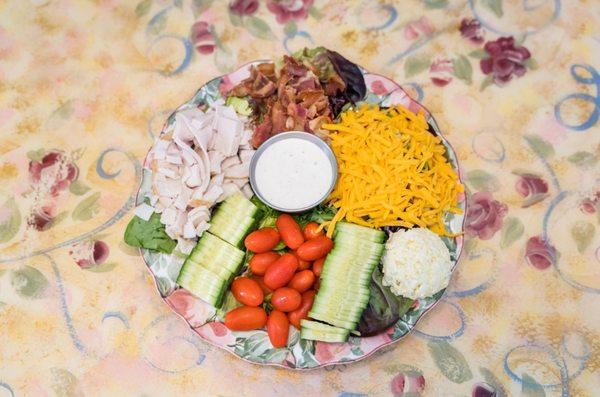 Tea Room Cobb Salad. Includes; A scoop of Egg Salad, Turkey, Ham, Bacon, Cheese, Tomatoes, Cucumbers and croutons on a bed of Spring mix.