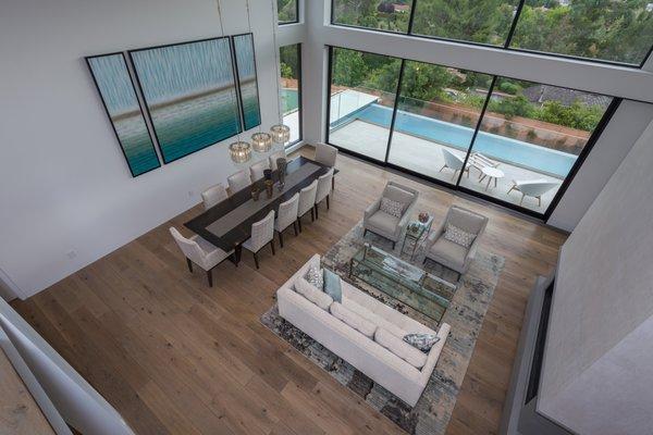 A helicopter view from the indoor balcony above, looking at the dining area with double height ceiling, wall to wall glass window.