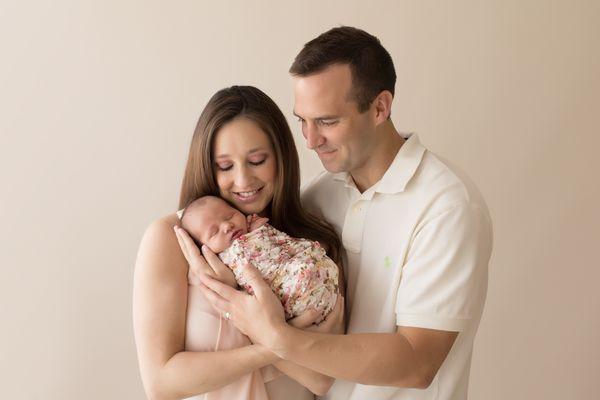 Mom and Dad portrait cuddling brand new newborn baby girl wearing neutral cream color and floral wrap Gainesville Florida