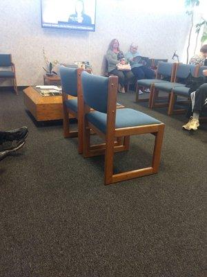 Uncomfortable waiting room with cheap uncomfortable chairs stacks of magazines my guess provided free from pharmacy companies.