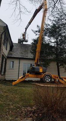 Our team using a lift to repair a chimney on a house with a slate roof.