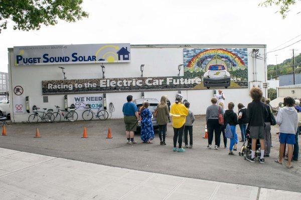 Racing To The Electric Car Future tile mural on our office wall over six free EV charging stations.